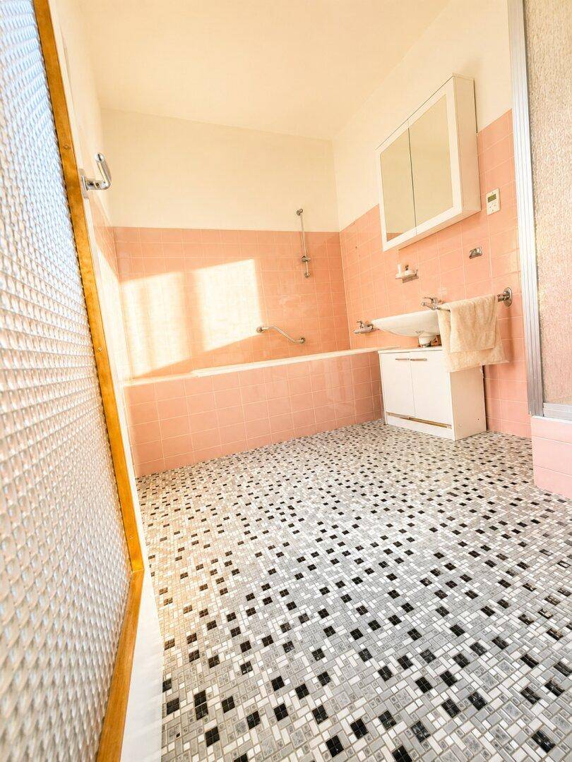 Badezimmer im 80er-Jahre-Stil mit rosa Fliesen, Badewanne und Mosaikboden.