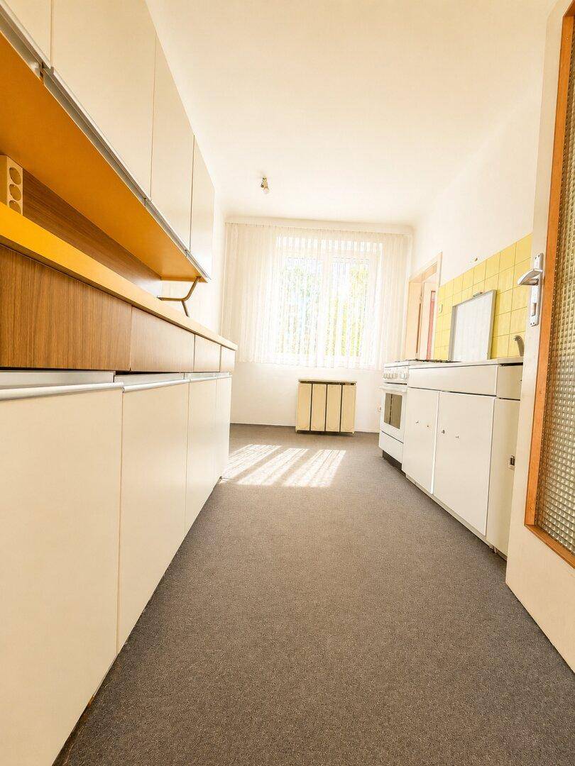 Helle Küche mit gelben Akzenten, weißer Einrichtung und einem Fenster, das viel Licht spendet.