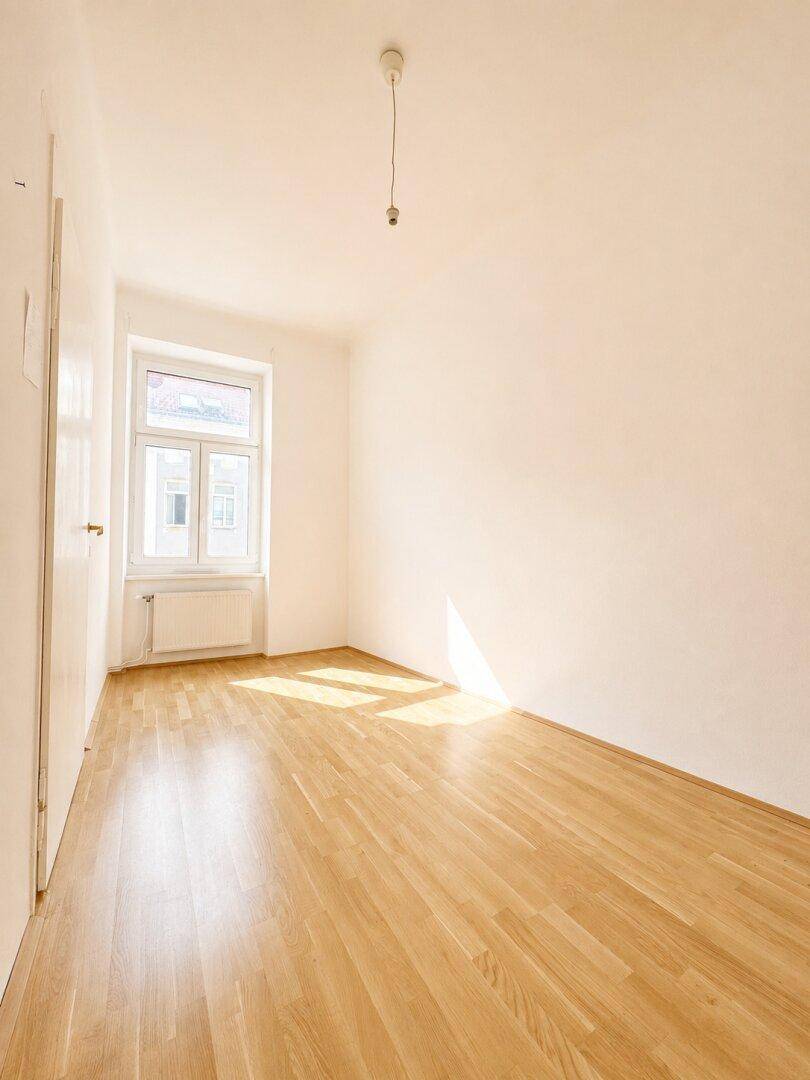 Helles Zimmer mit Parkettboden und einem Fenster, ideal als Schlaf- oder Arbeitszimmer.