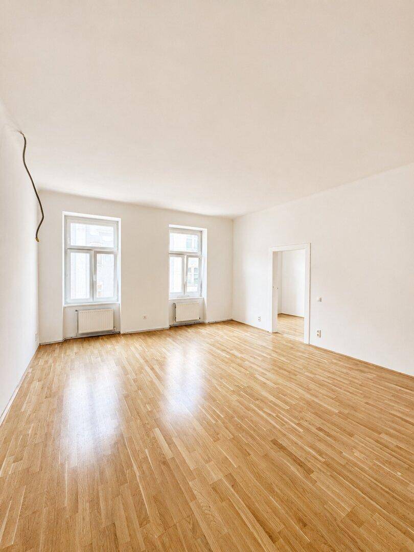 Großes, leeres Zimmer mit Parkettboden und zwei Fenstern, bereit zur individuellen Gestaltung.