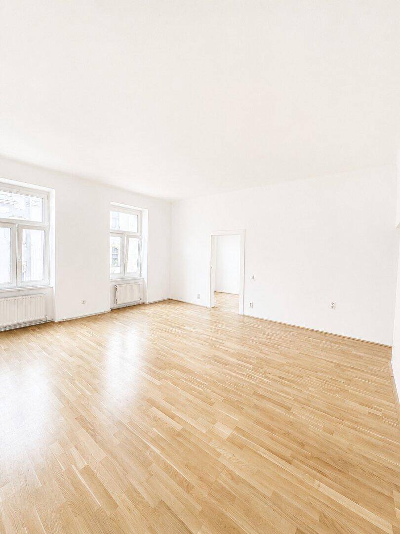 Geräumiges, helles Zimmer mit Parkettboden und zwei großen Fenstern.
