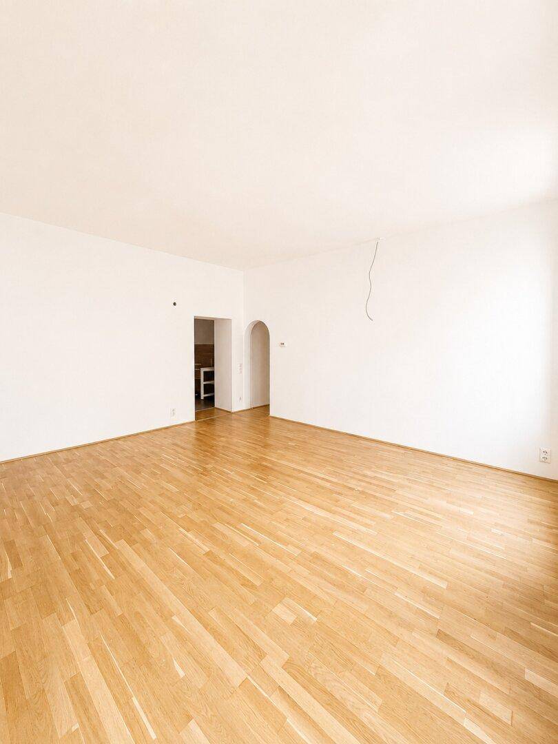 Geräumiges Zimmer mit Parkettboden und Zugang zu einem weiteren Raum.