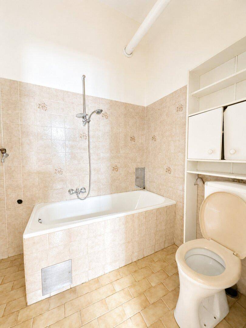 Badezimmer mit Badewanne, Duschvorrichtung und Toilette, ausgestattet mit beigefarbenen Fliesen.