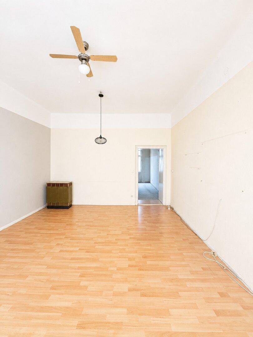 Geräumiges, leeres Zimmer mit hellem Parkettboden und Deckenventilator, mit Zugang zu einem weiteren Raum.