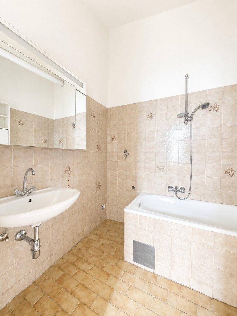 Funktionales Badezimmer mit Badewanne, Waschbecken, Spiegelschrank und beigefarbenen Wand- und Bodenfliesen.