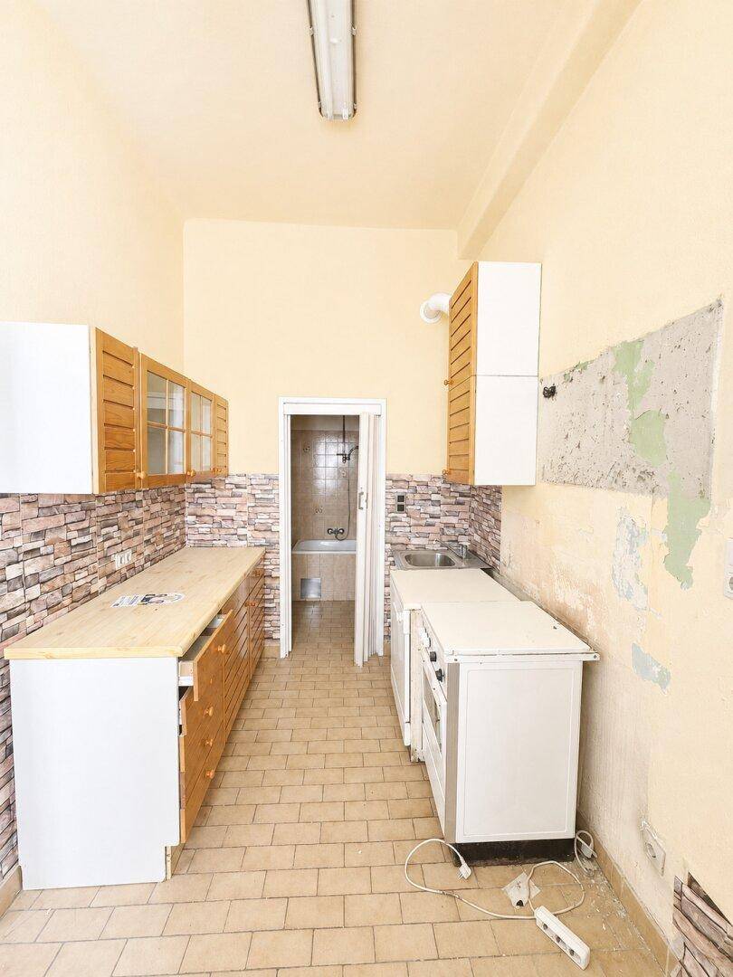 Renovierungsbedürftige Küche mit alten Einbauschränken, Fliesenboden und Zugang zu einem Badezimmer.
