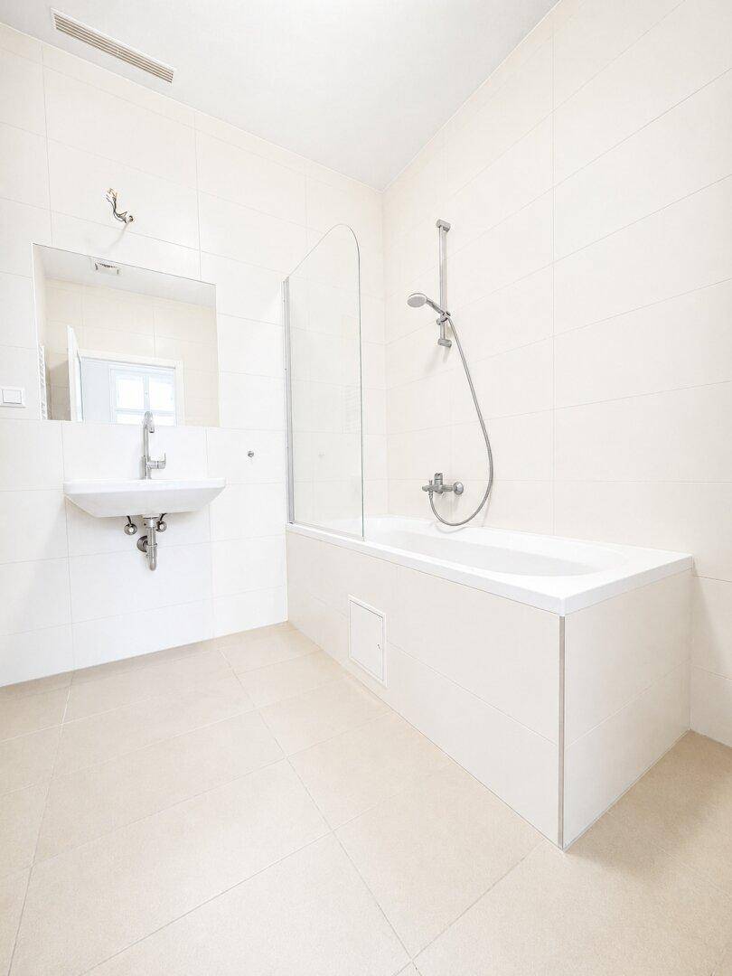 Modernes Badezimmer mit Badewanne, Duschvorrichtung und weißen Fliesen.