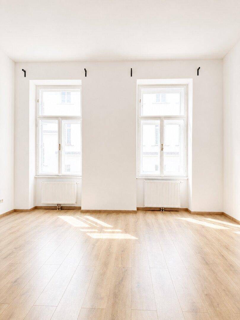 Lichtdurchfluteter Raum mit Laminatboden und zwei hohen Fenstern.