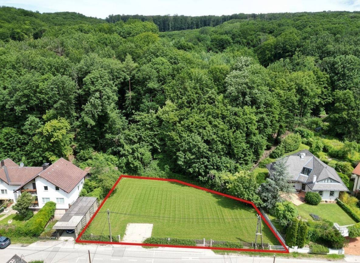 Luftaufnahme eines Grundstücks mit roter Umrandung, umgeben von Wald und Häusern.