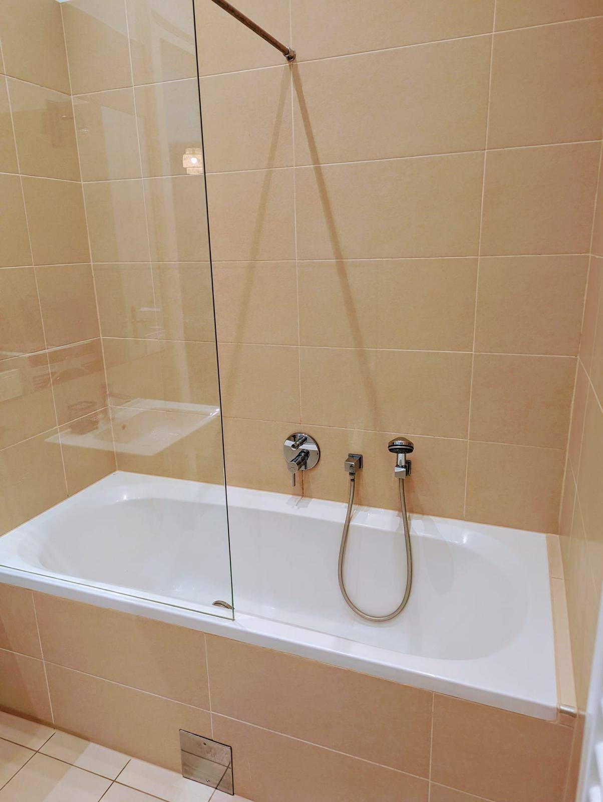 Badewanne mit Duschabtrennung aus Glas in einem gefliesten Badezimmer.
