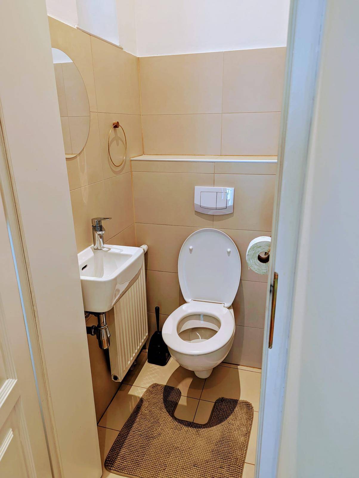 Kleines Gäste-WC mit beigefarbenen Fliesen, wandhängendem WC und kleinem Waschbecken.