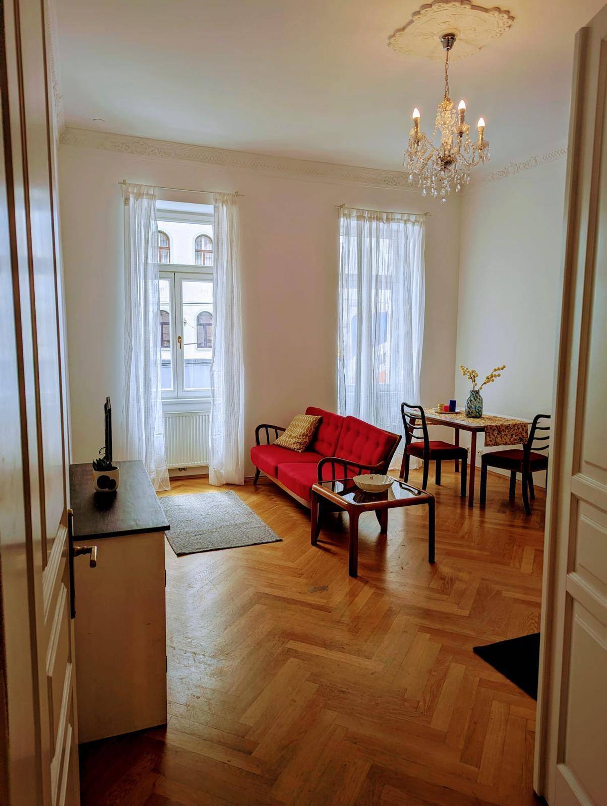 Gemütlicher Wohn-Essbereich mit rotem Sofa, Esstisch und Fischgrätparkett, durch hohe Fenster hell.