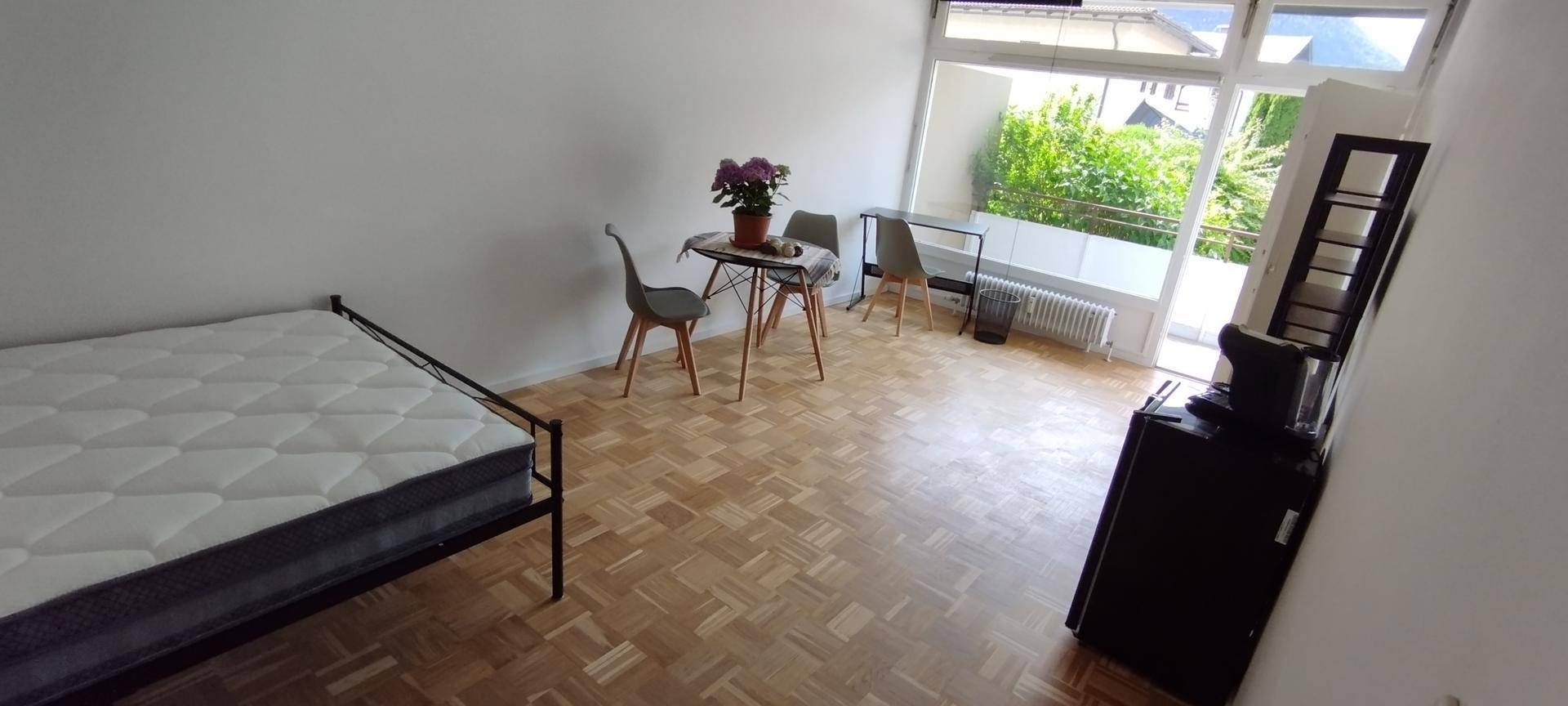 Heller Wohnraum mit Parkettboden, Bett, Esstisch und Zugang zum Balkon.