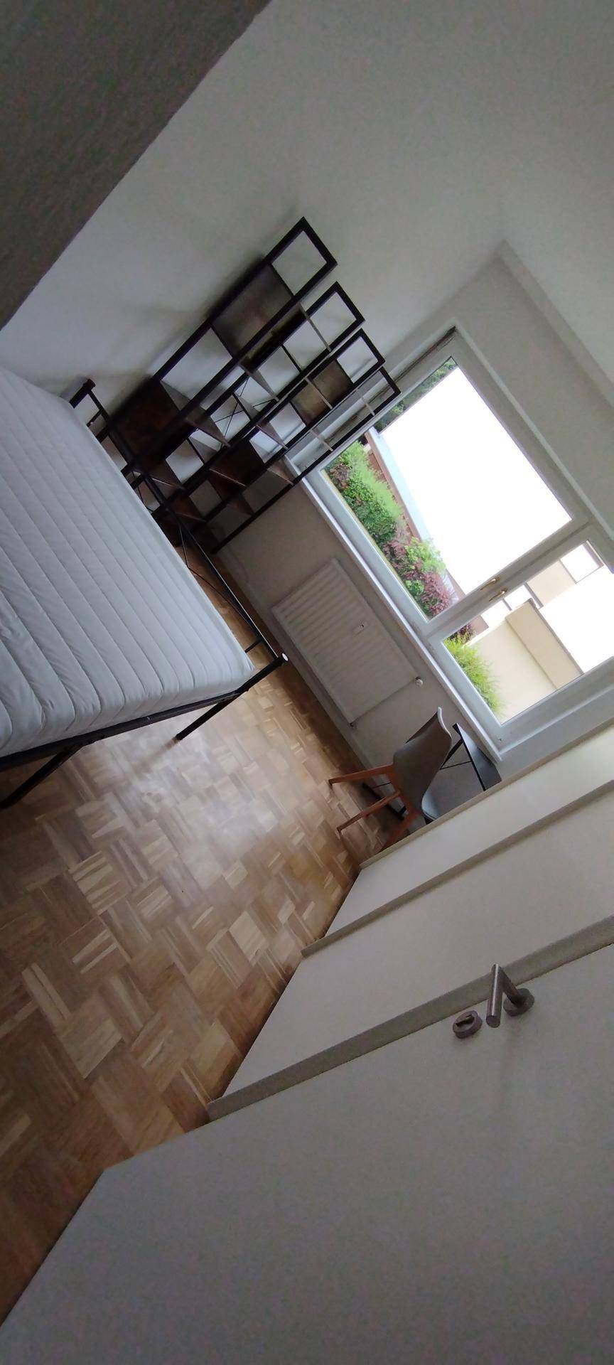 Schlafzimmer mit Parkettboden, einem Bett und einem Regal, mit Blick auf das Fenster.