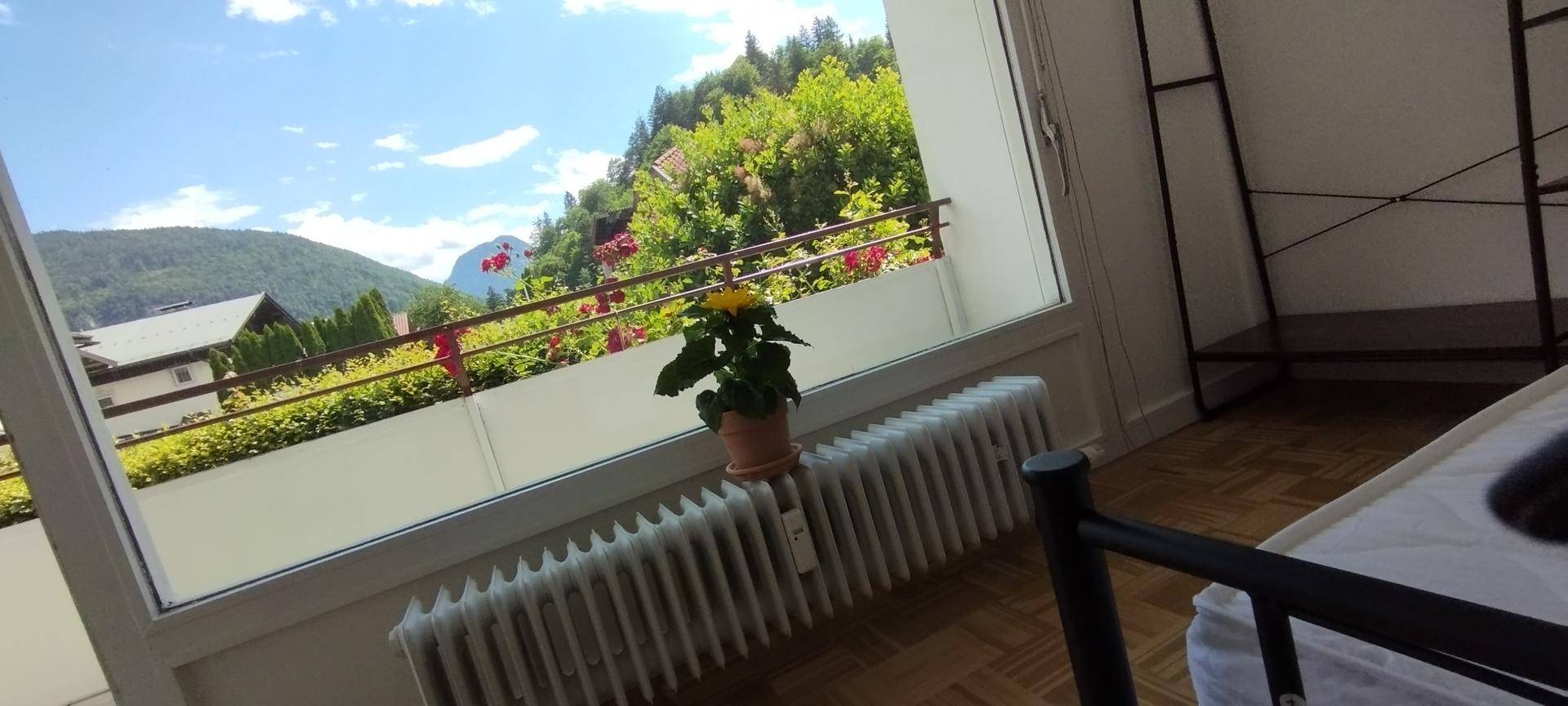 Schlafzimmer mit Balkonzugang, Parkettboden und weitem Blick auf die Berge und grüne Landschaft.