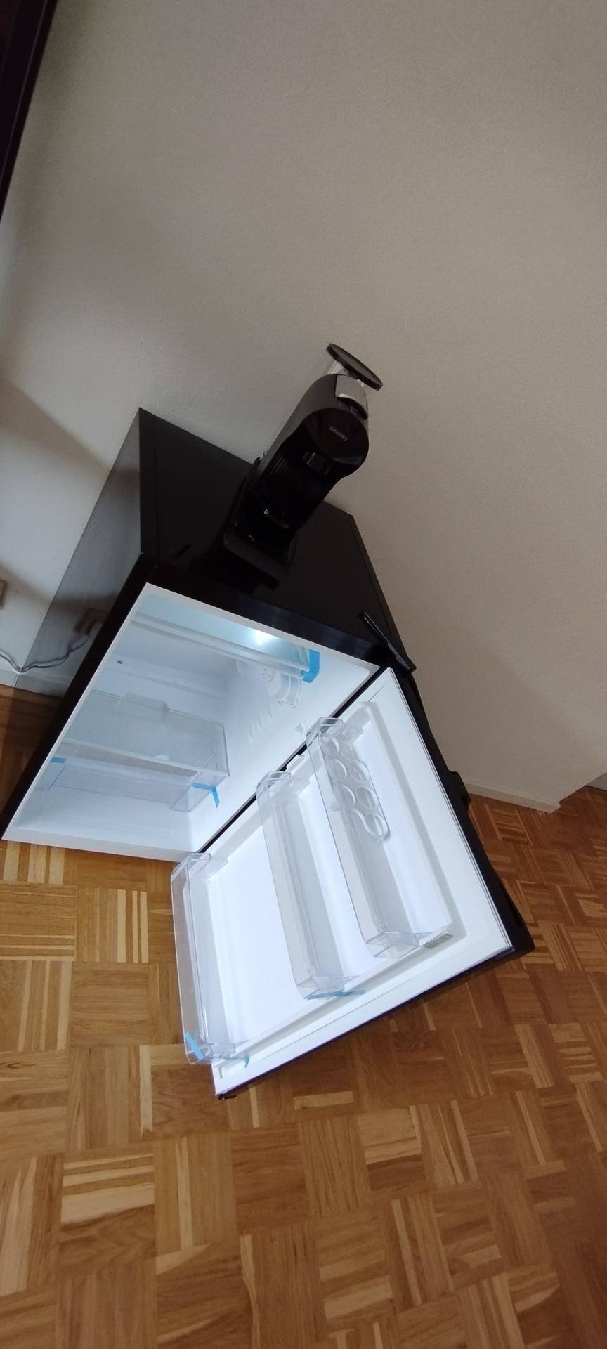 Kleiner Kühlschrank mit offener Tür in einem hellen Wohnraum.