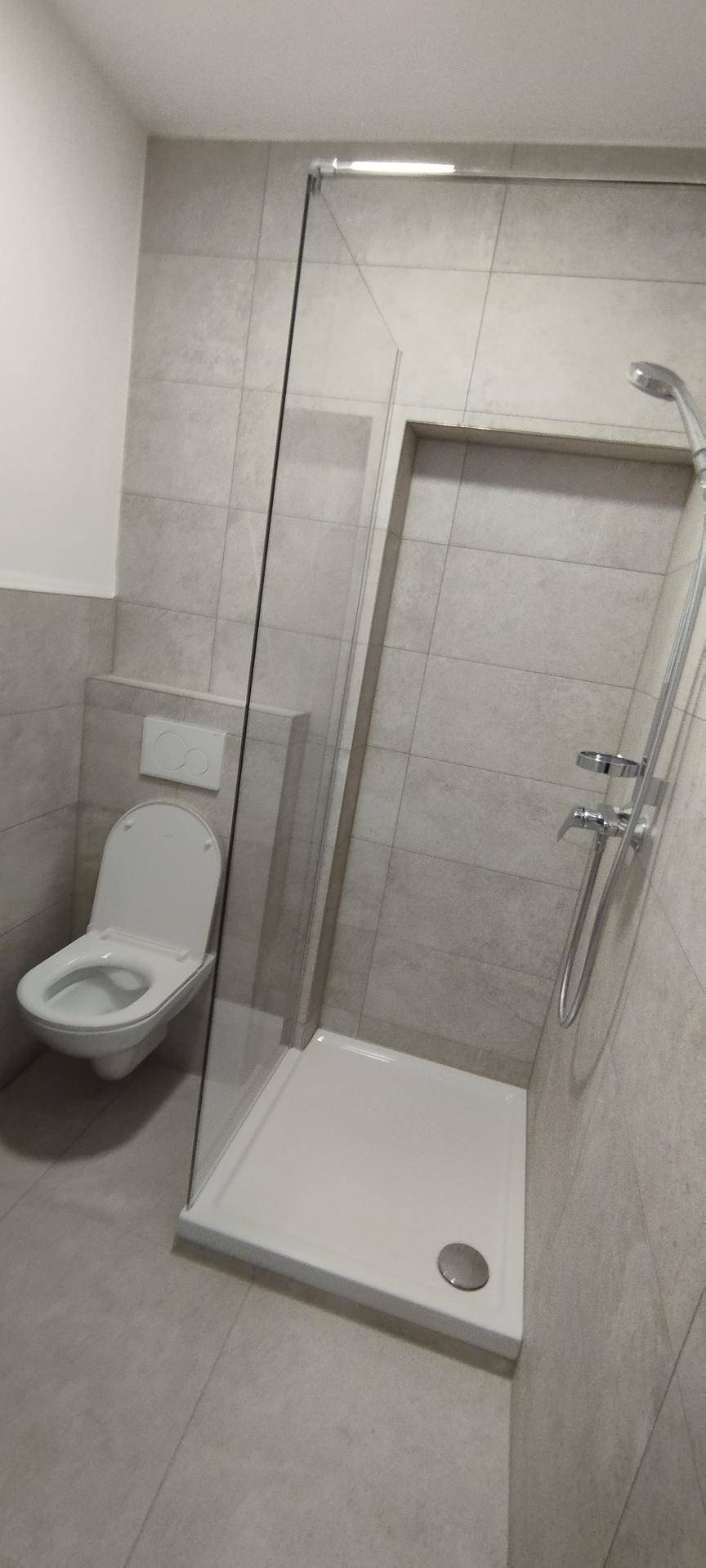 Modernes Badezimmer mit Dusche, WC und grauen Fliesen.