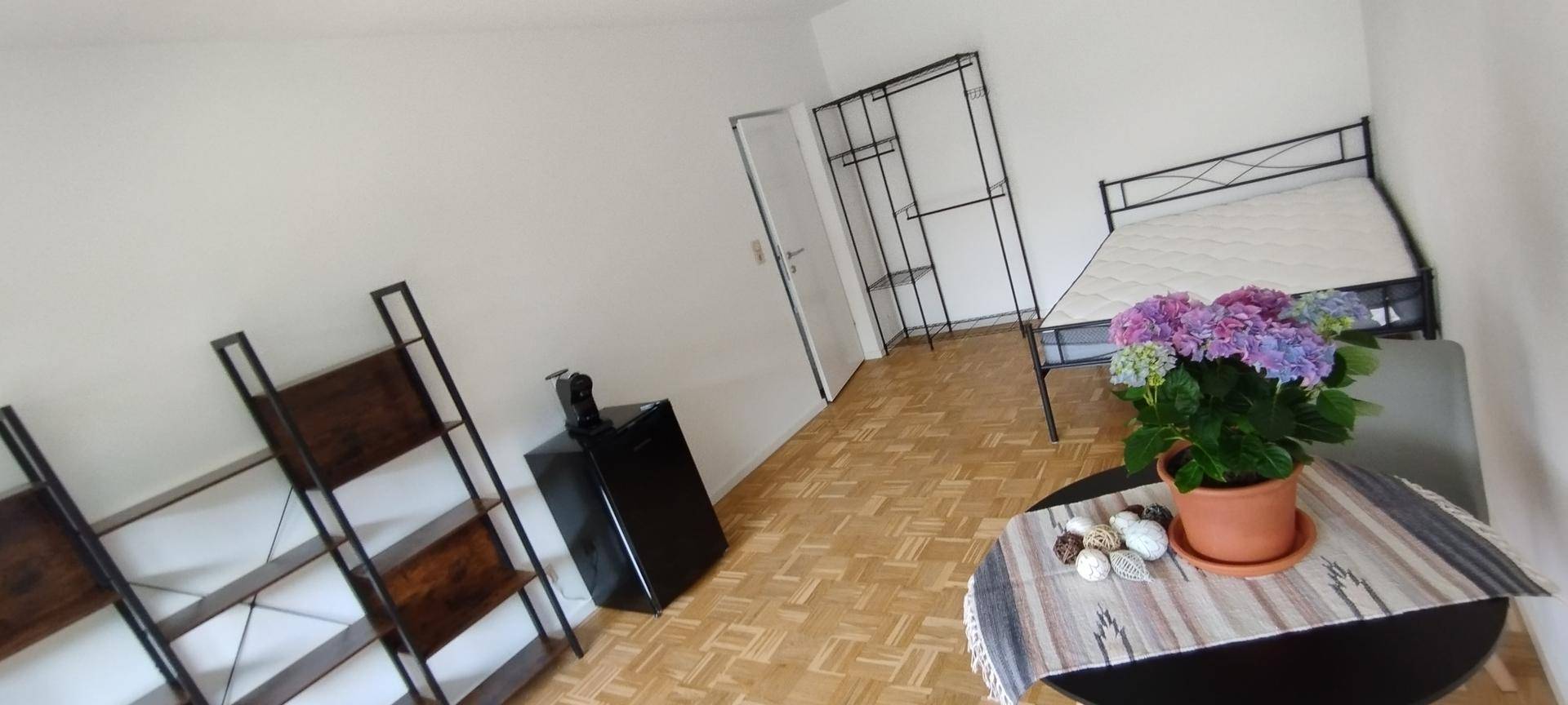 Heller Wohnraum mit Parkettboden, Bett und Topfpflanze.