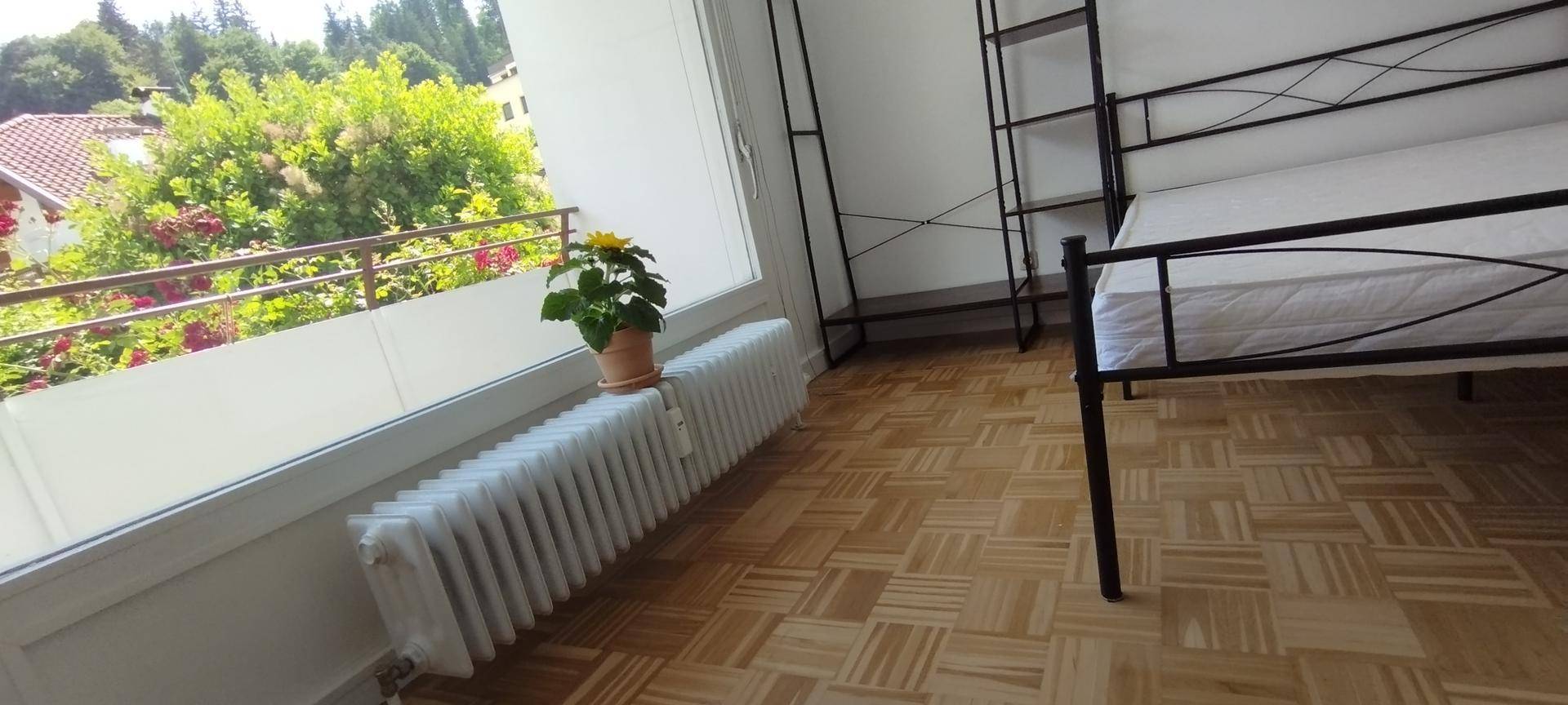 Schlafzimmer mit Parkettboden, einem Bettgestell und Zugang zu einem Balkon mit grüner Aussicht.