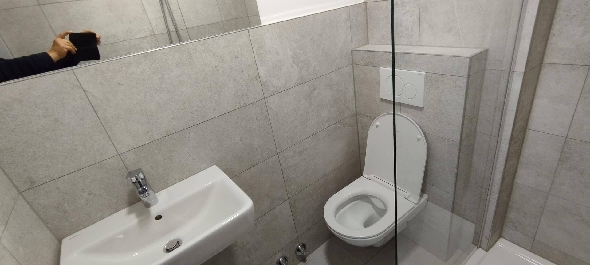 Modernes Badezimmer mit grauen Fliesen, wandhängendem WC und einem Waschbecken.
