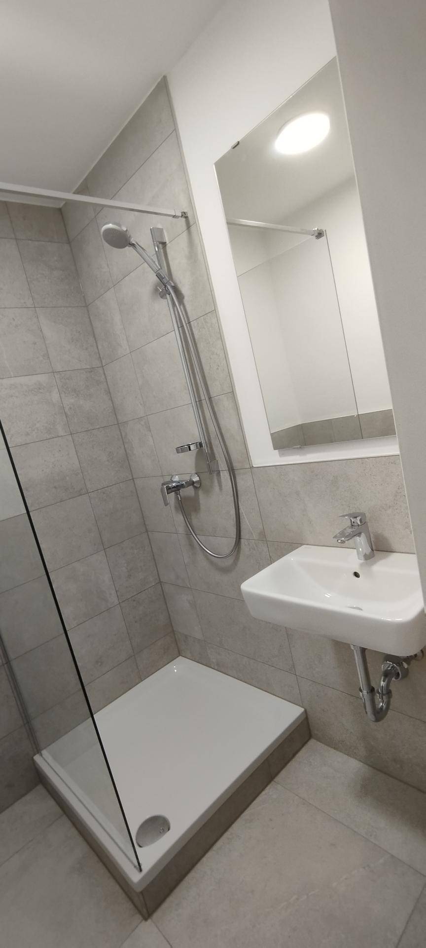 Funktionales Badezimmer mit Duschbereich, Waschbecken und einem Spiegel.