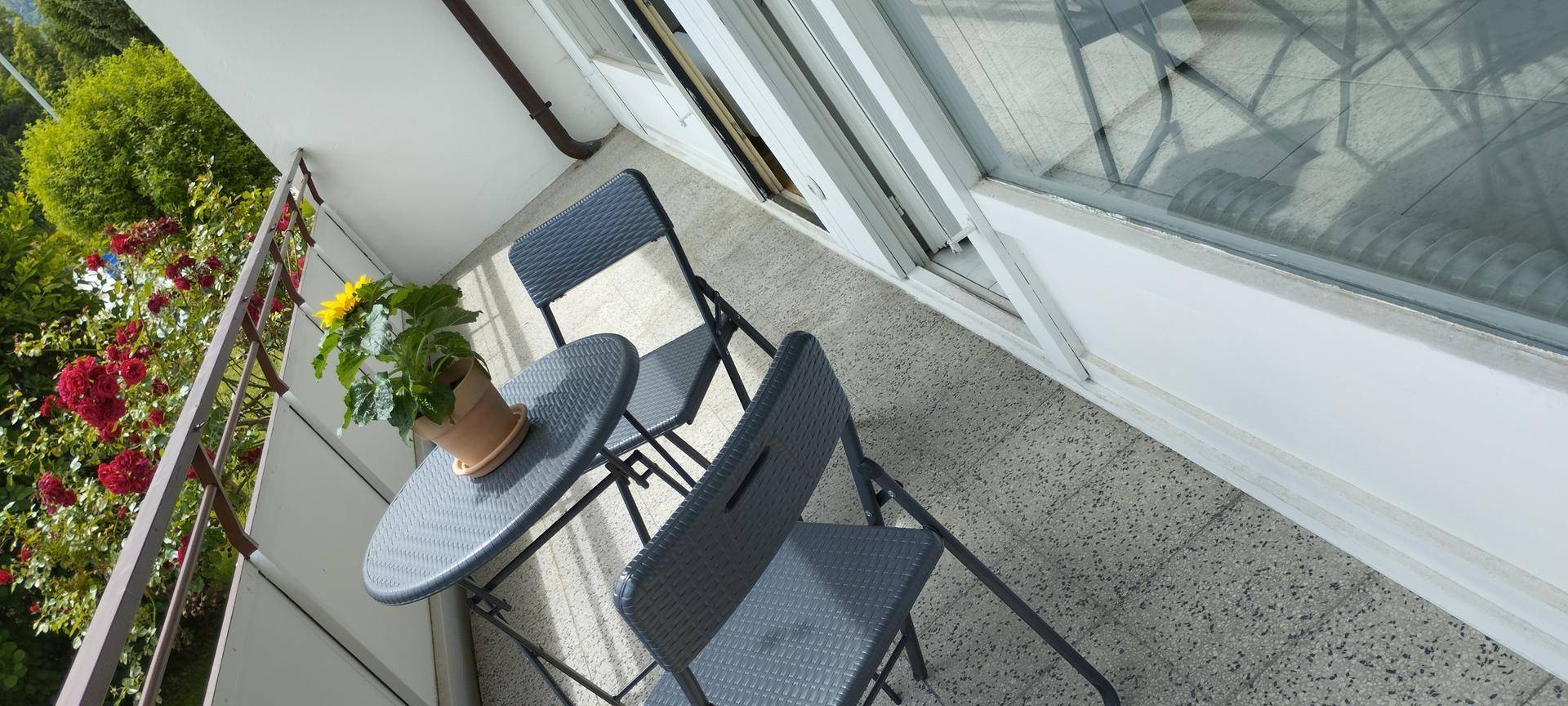 Kleiner Balkon mit Sitzgelegenheiten und einer Topfpflanze, umgeben von üppigem Grün.