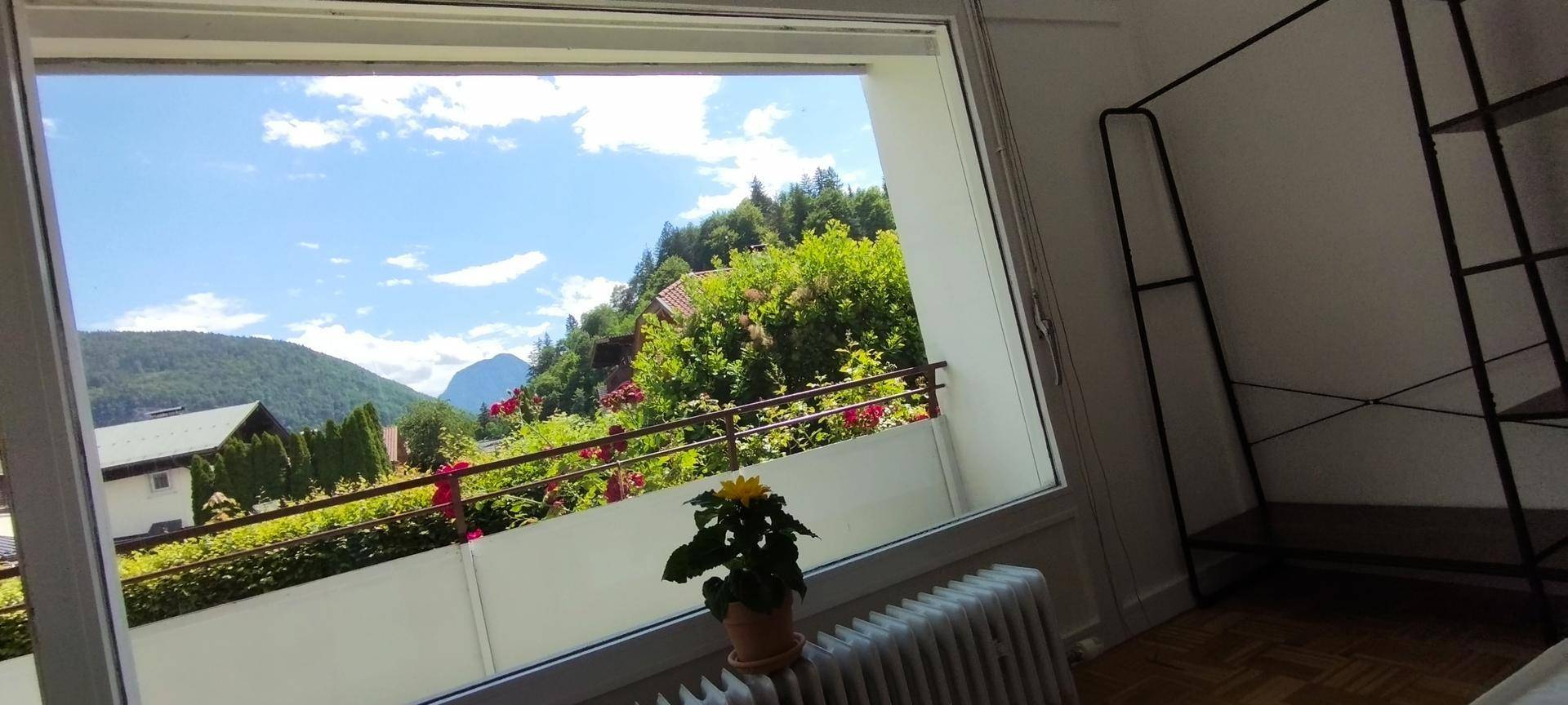 Helles Schlafzimmer mit Balkonzugang und Panoramablick auf die umliegende Berglandschaft und den blauen Himmel.