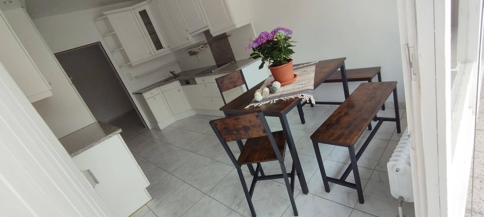 Helle Küche mit weißen Schränken, Granitarbeitsplatten und einem Essbereich mit Holztisch und Bänken.