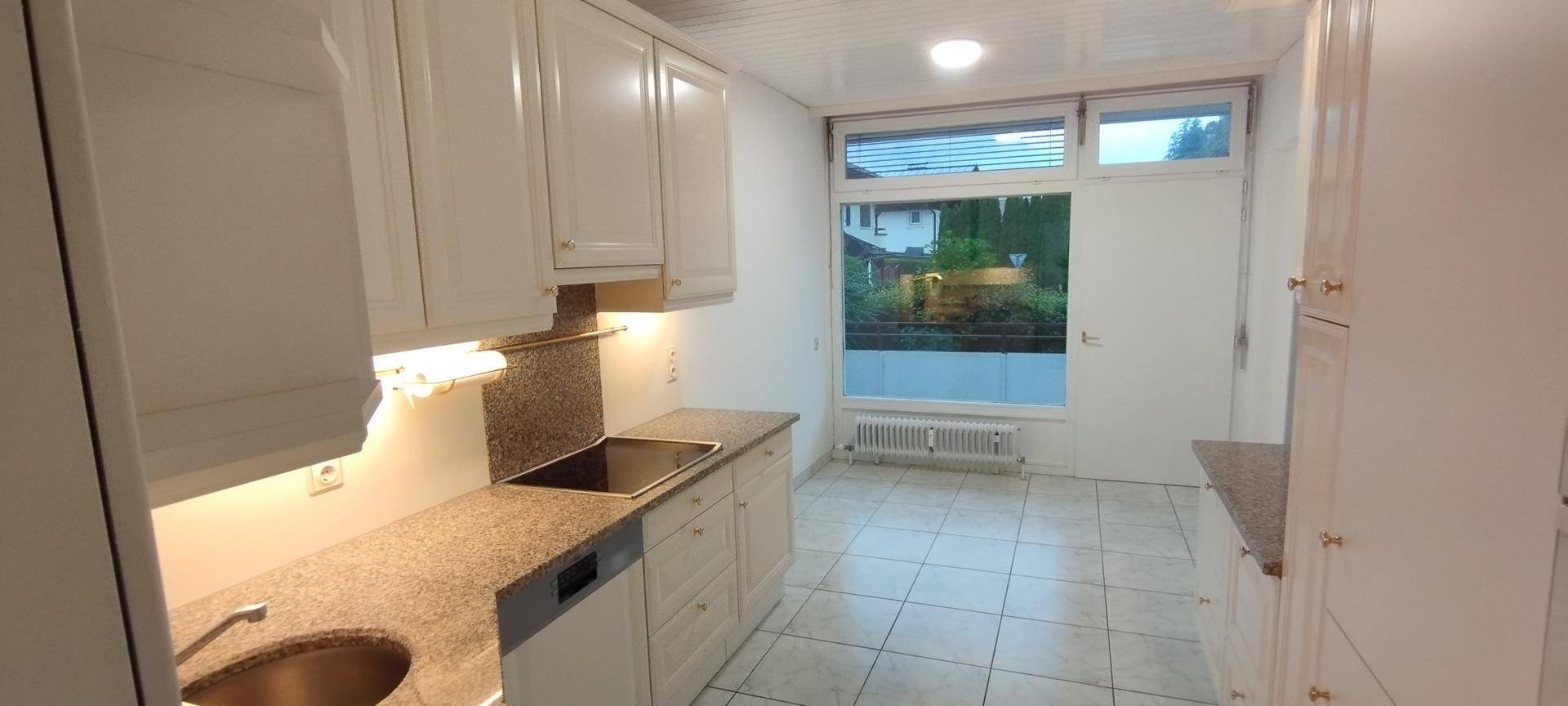 Funktionale Küche mit weißen Einbauschränken, Granitarbeitsplatten und einem Fenster für Tageslicht.