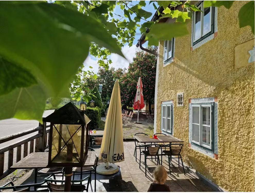Sonniger Terrassenbereich mit Tischen, Stühlen und Sonnenschirmen neben einem traditionellen Gebäude.
