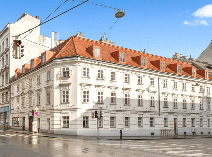 Historisches Eckgebäude mit klassischer Fassade, vielen Fenstern und Mansarddach in der Stadt.
