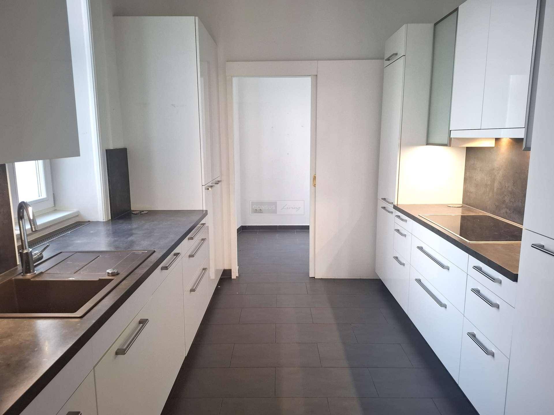 Moderne Küche mit weißen Schränken, dunklen Arbeitsplatten und integriertem Spülbereich.