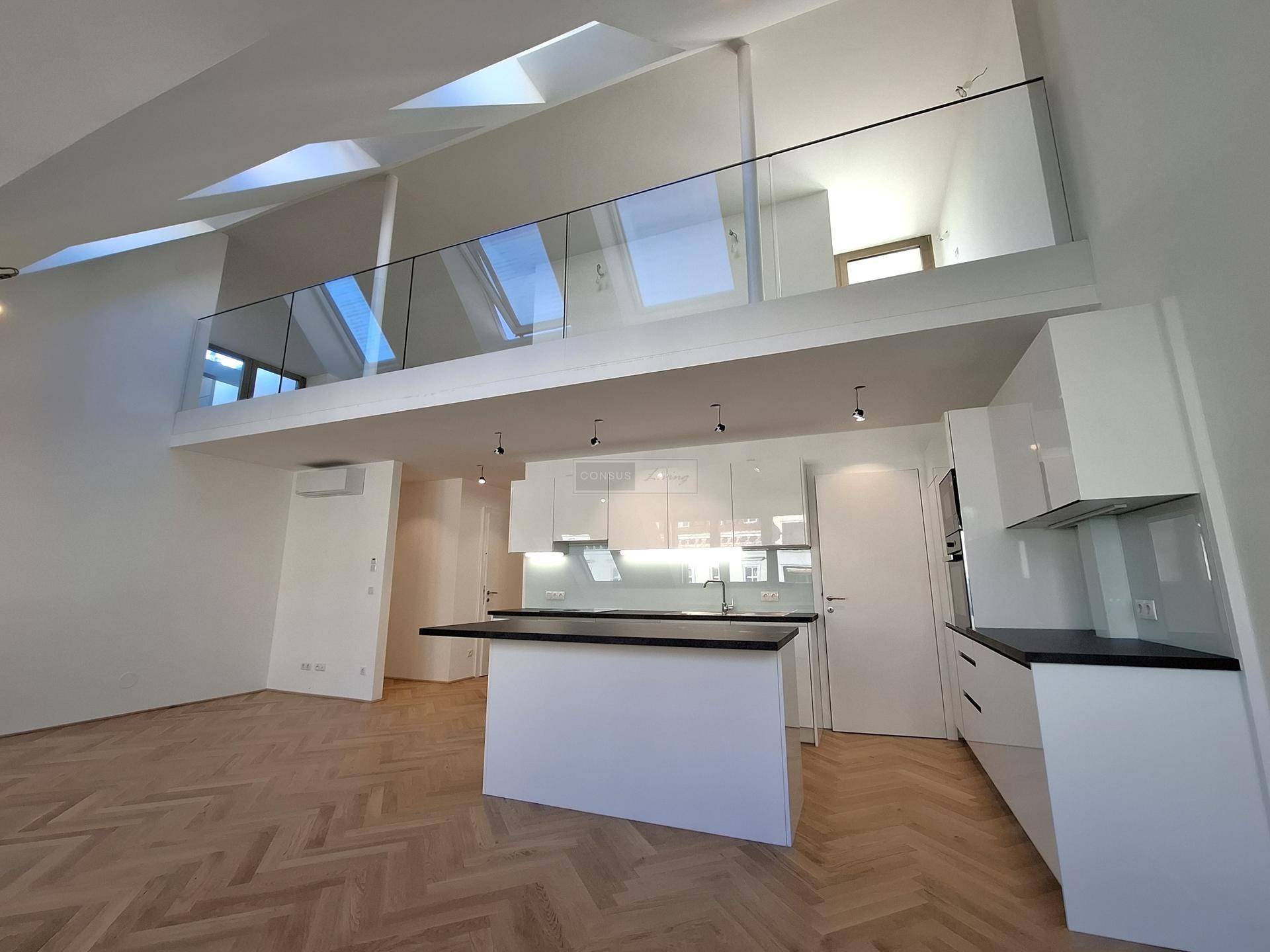 Helle Küche mit Kochinsel und Blick auf die offene Galerie mit Glasgeländer und hohen Decken.