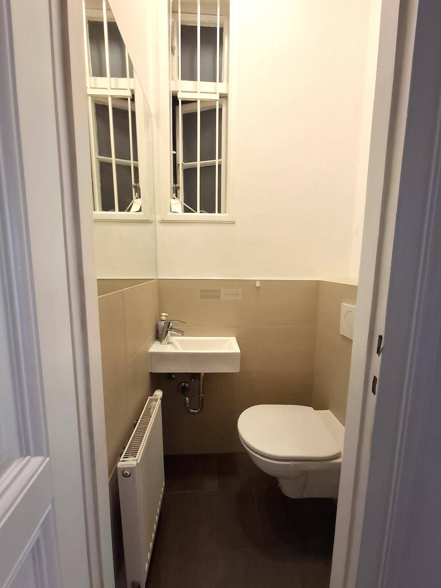 Kompaktes Gäste-WC mit wandhängender Toilette, kleinem Waschbecken und Fenster für Belüftung.