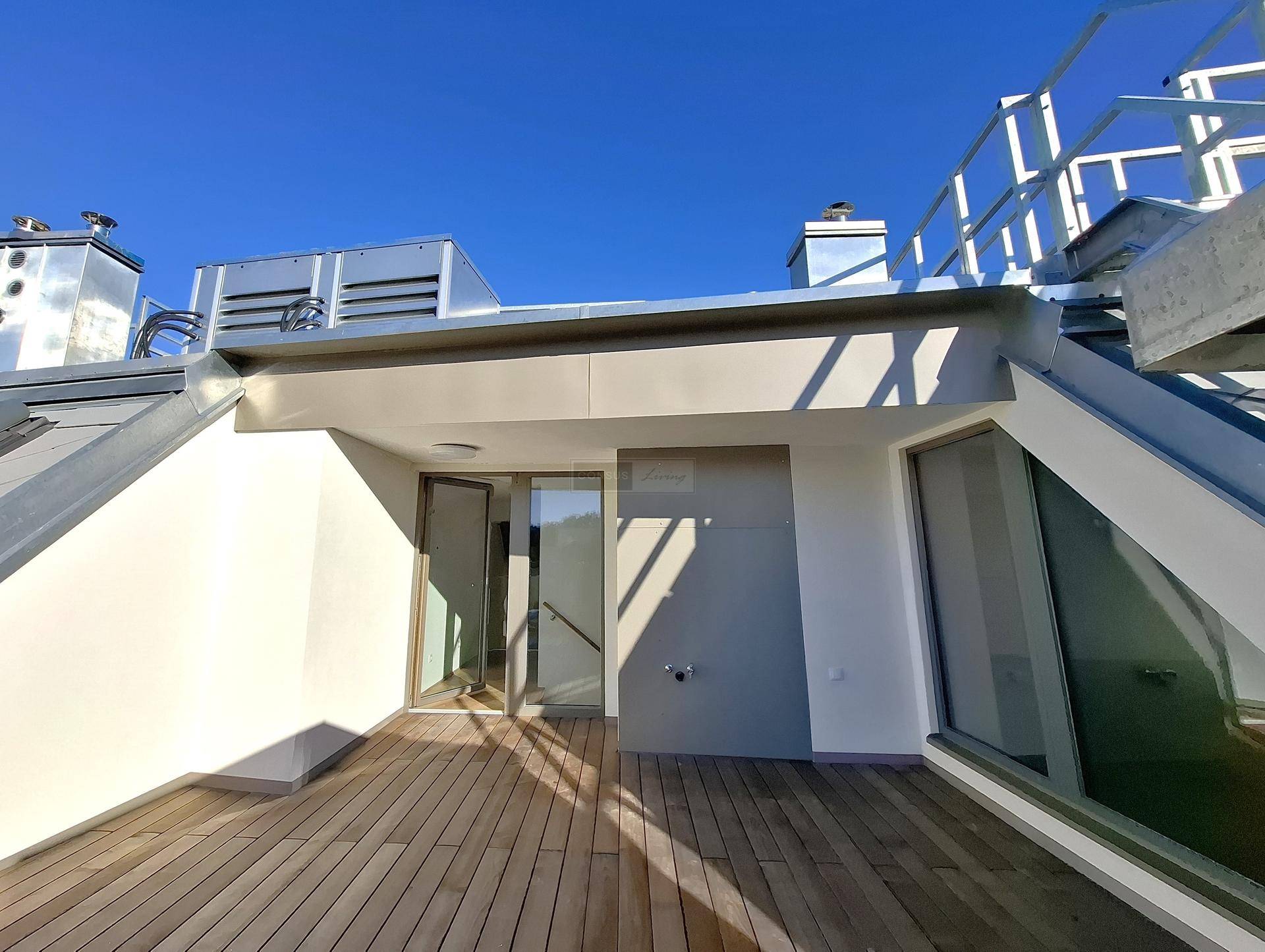 Heller Zugang zur Dachterrasse mit Holzboden und moderner Architektur unter blauem Himmel.