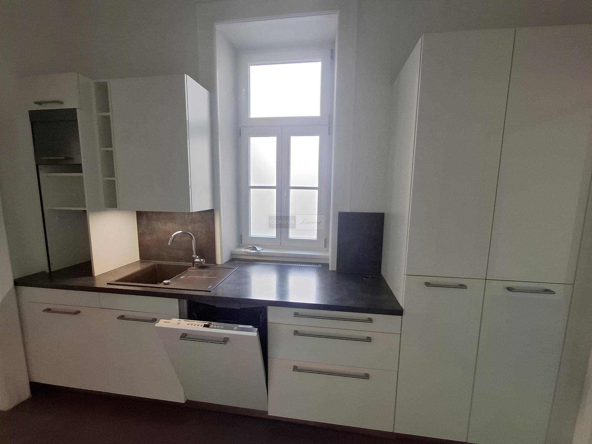 Funktionale Küche mit weißen Schränken, Spülbecken und integriertem Geschirrspüler unter dem Fenster.
