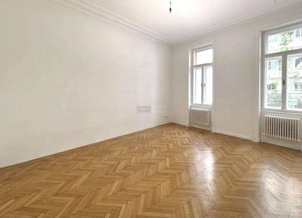 Heller Wohnraum mit klassischem Fischgrätparkett, hohen Decken und großen Fenstern, die viel Tageslicht hereinlassen.