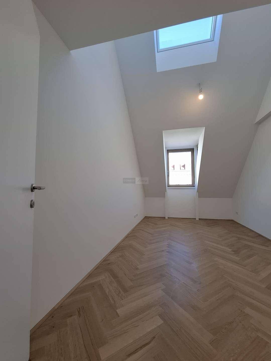 Helles Zimmer im Dachgeschoss mit Fischgrätparkett, Dachfenster und schrägen Wänden.