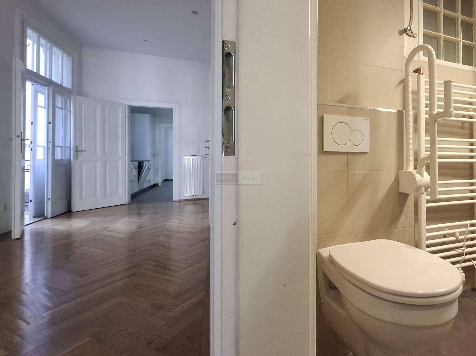 Badezimmer mit Toilette und Handtuchheizkörper, mit Blick in einen angrenzenden Raum mit Parkett.
