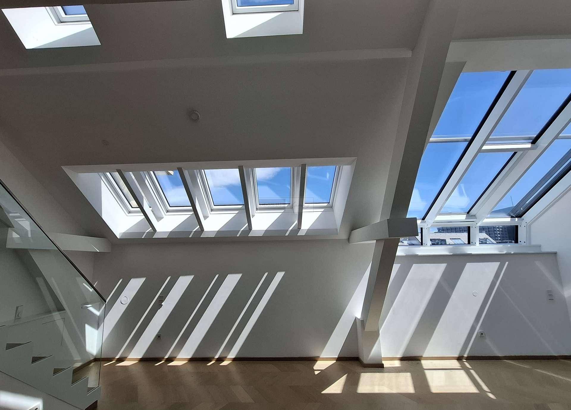 Lichtdurchfluteter Raum im Dachgeschoss mit vielen Dachfenstern und Holzbalken.