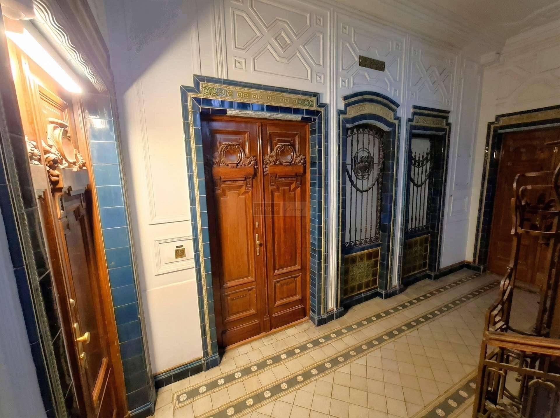 Prunkvoller Eingangsbereich mit kunstvollen Holztüren, dekorativen Fliesen und aufwendigen Metallarbeiten in einem Altbau.