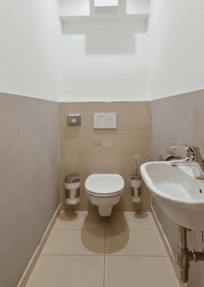 Kompaktes Gäste-WC mit Wand-WC, kleinem Waschbecken und hellen Fliesen.