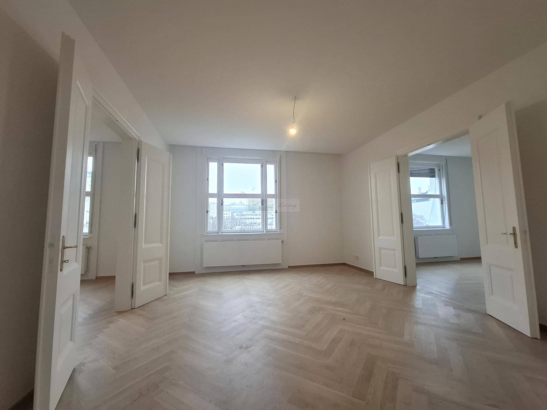 Großes, helles Zimmer mit Fischgrätparkett und Fenstern, die einen Blick auf die Stadt bieten.