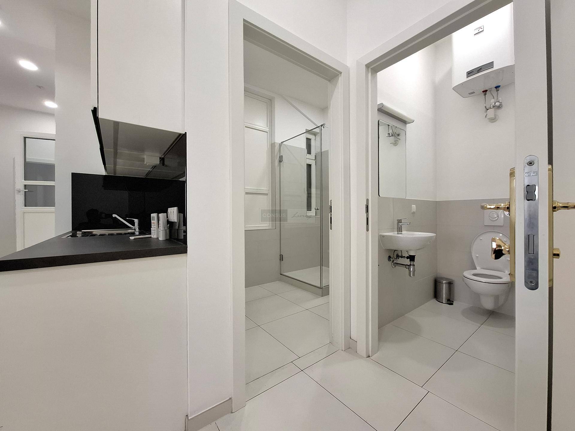 Flur mit Zugang zu einer modernen Dusche und einer separaten Toilette, alles mit hellen Fliesen.