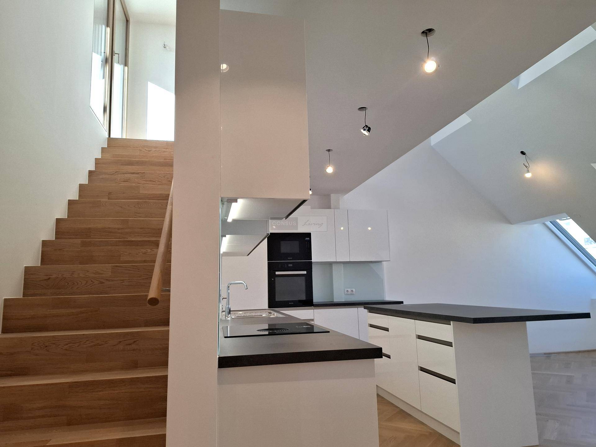 Moderne Einbauküche mit weißen Hochglanzfronten und Holztreppe, die zum oberen Bereich führt.