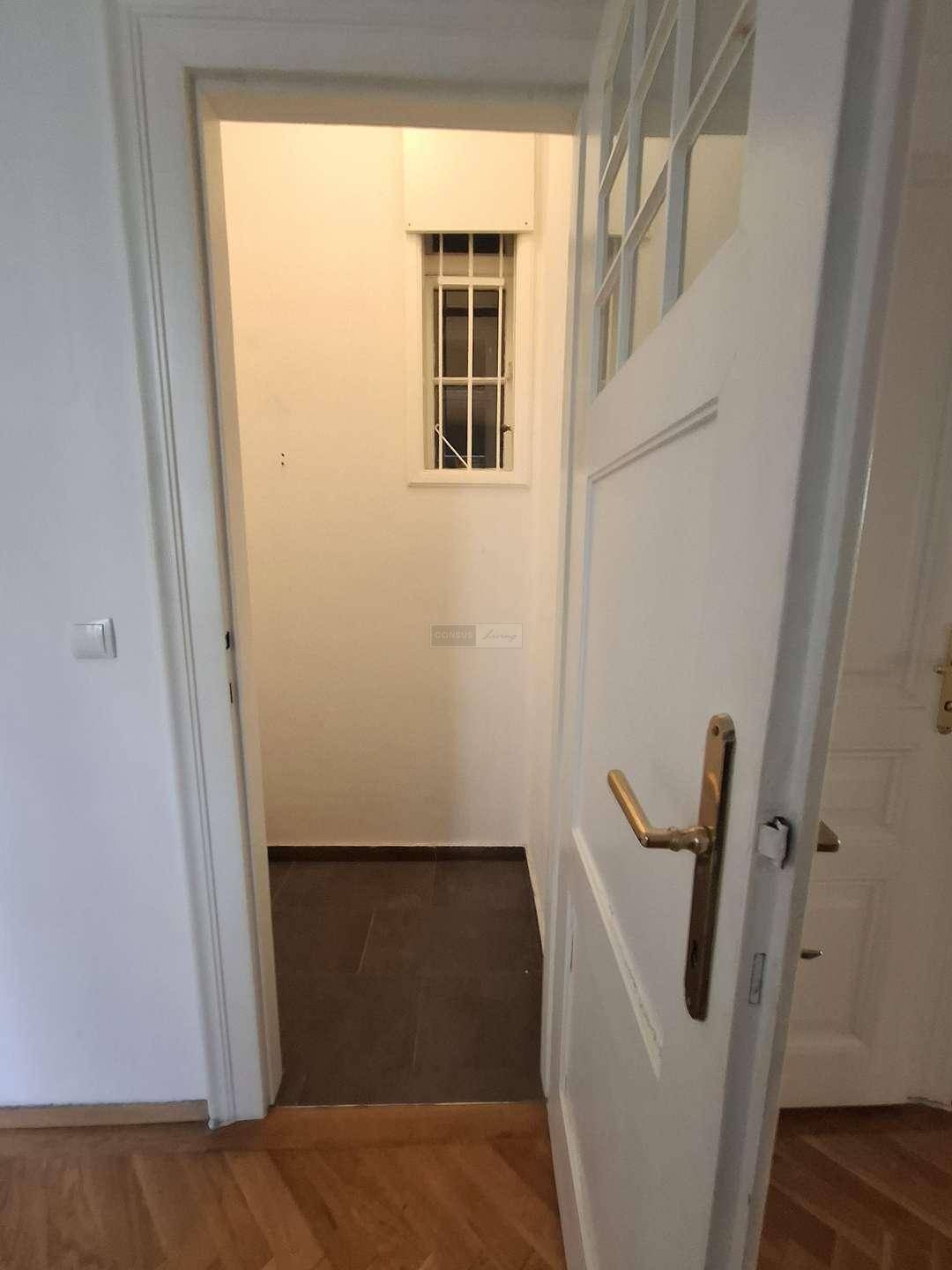 Schmaler Raum mit dunklen Fliesen und einem vergitterten Fenster, ideal als Abstellkammer.