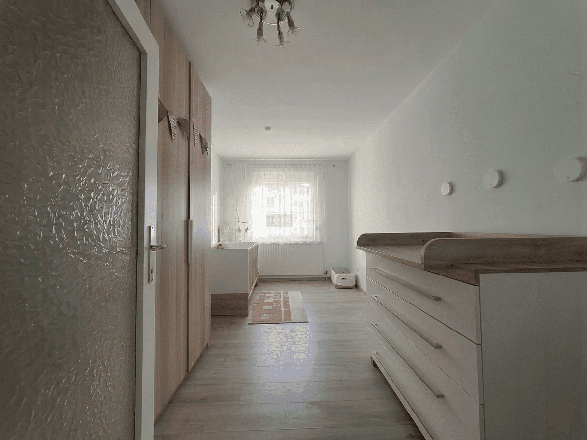 Helles Schlafzimmer mit Wickelkommode, großem Kleiderschrank und Fenster.