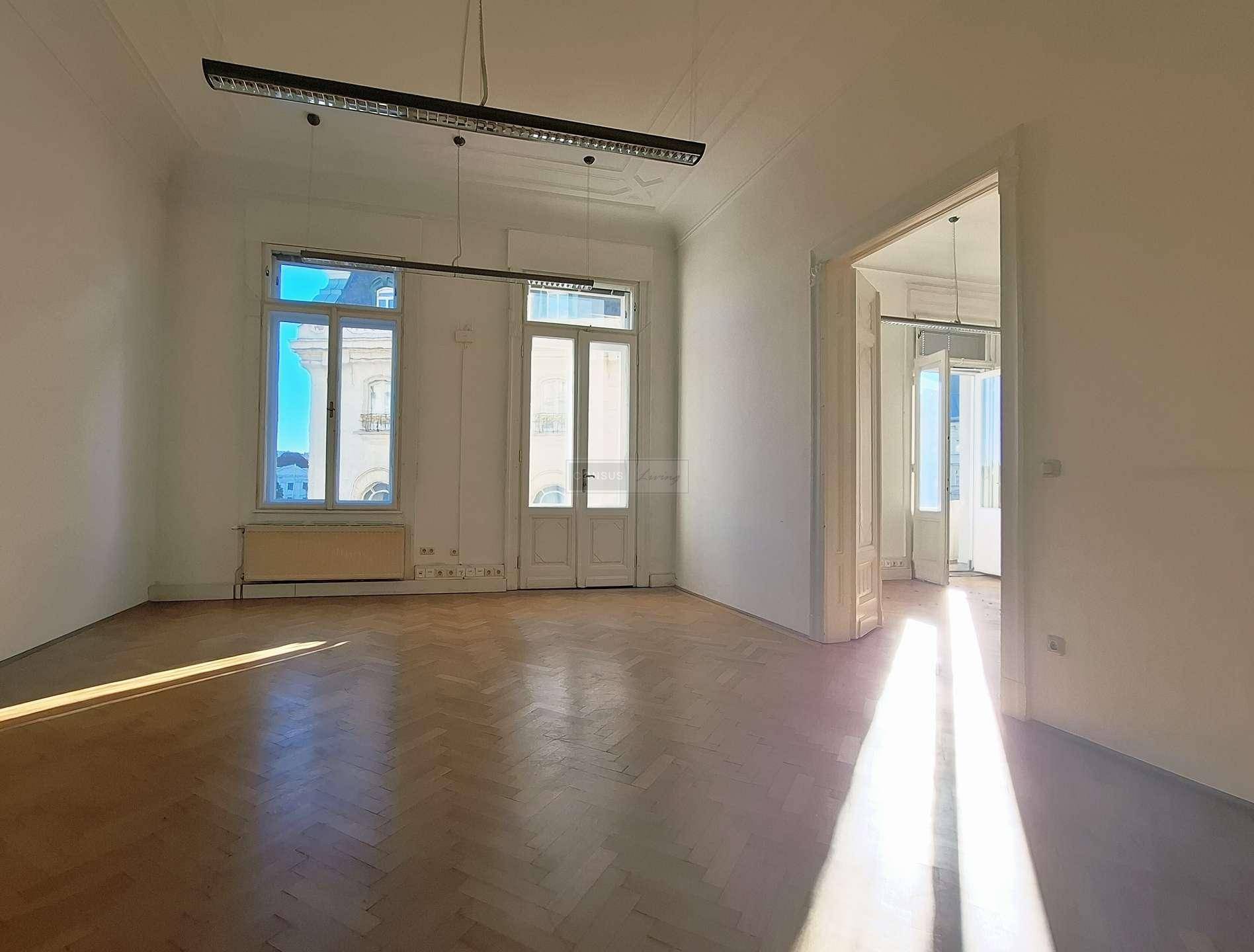 Heller, leerer Raum mit elegantem Fischgrätparkett, hohen Decken und großen Fenstern, die den Raum mit Sonnenlicht füllen.