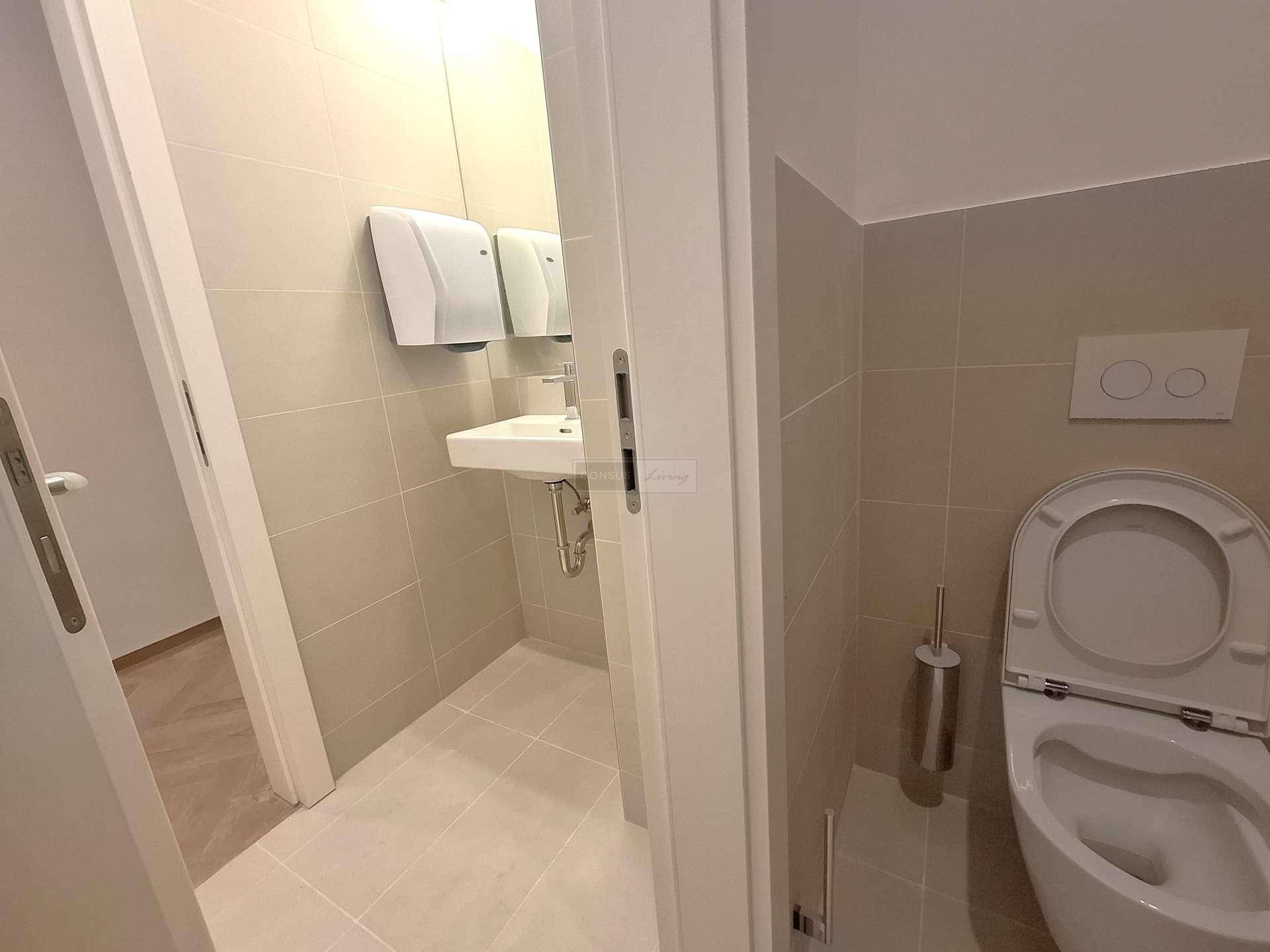 Modernes Gäste-WC mit hellen Fliesen, wandhängendem WC und kleinem Waschbecken.