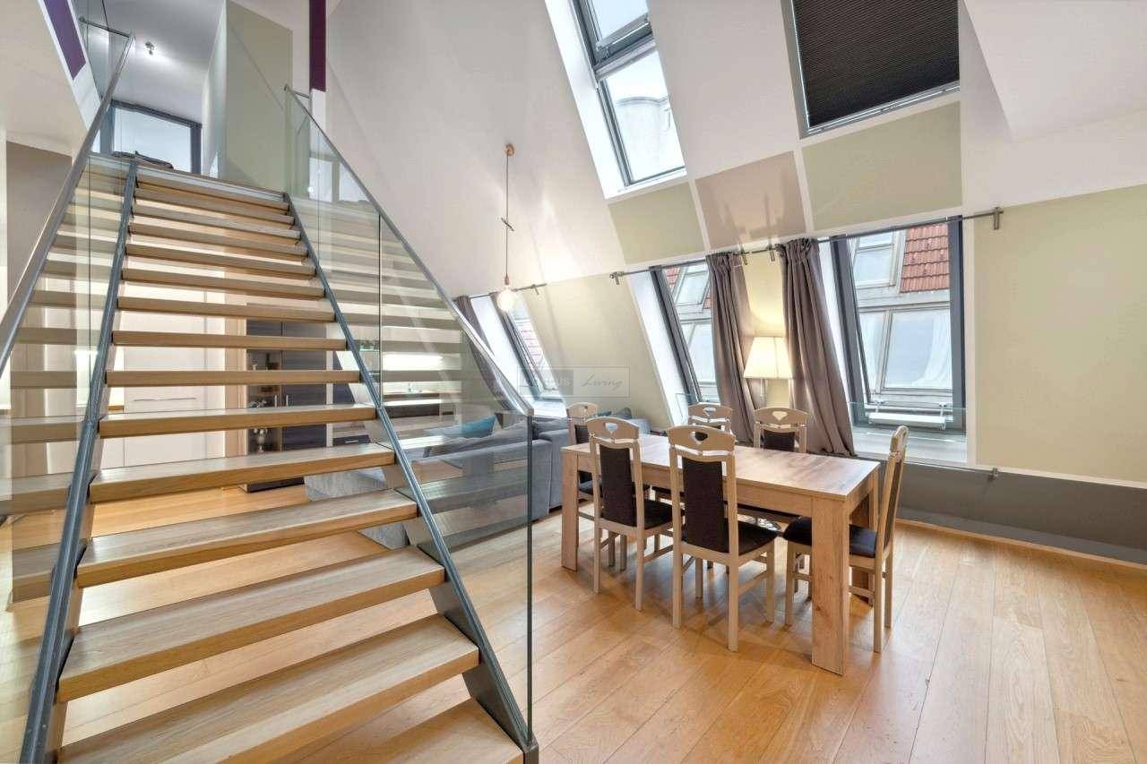 Geräumiger Essbereich mit Holztisch, Parkettboden und moderner Treppe mit Glasgeländer.